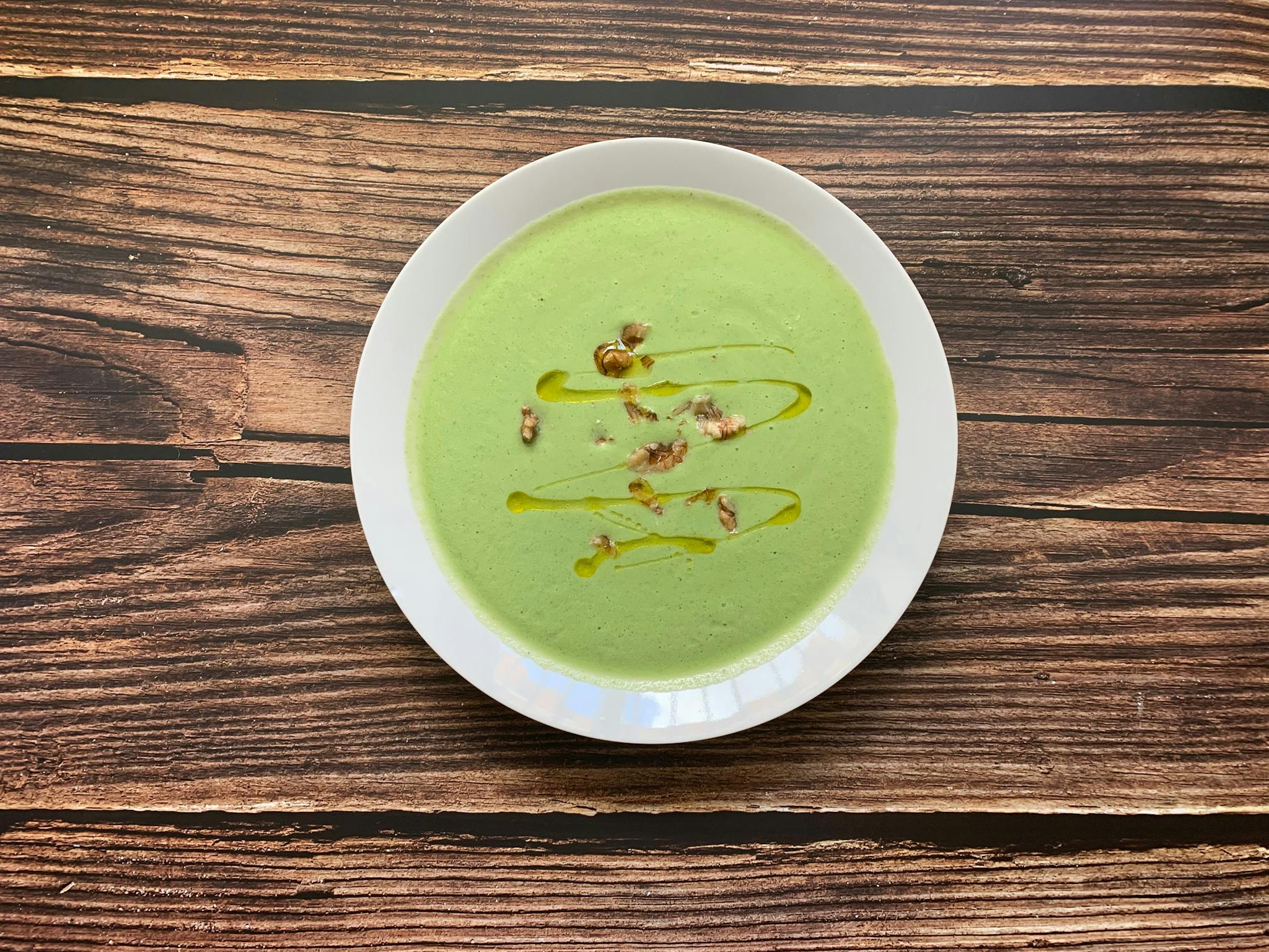A delicious creamy broccoli soup garnished with walnuts and olive oil, served in a white bowl on a rustic wooden table.