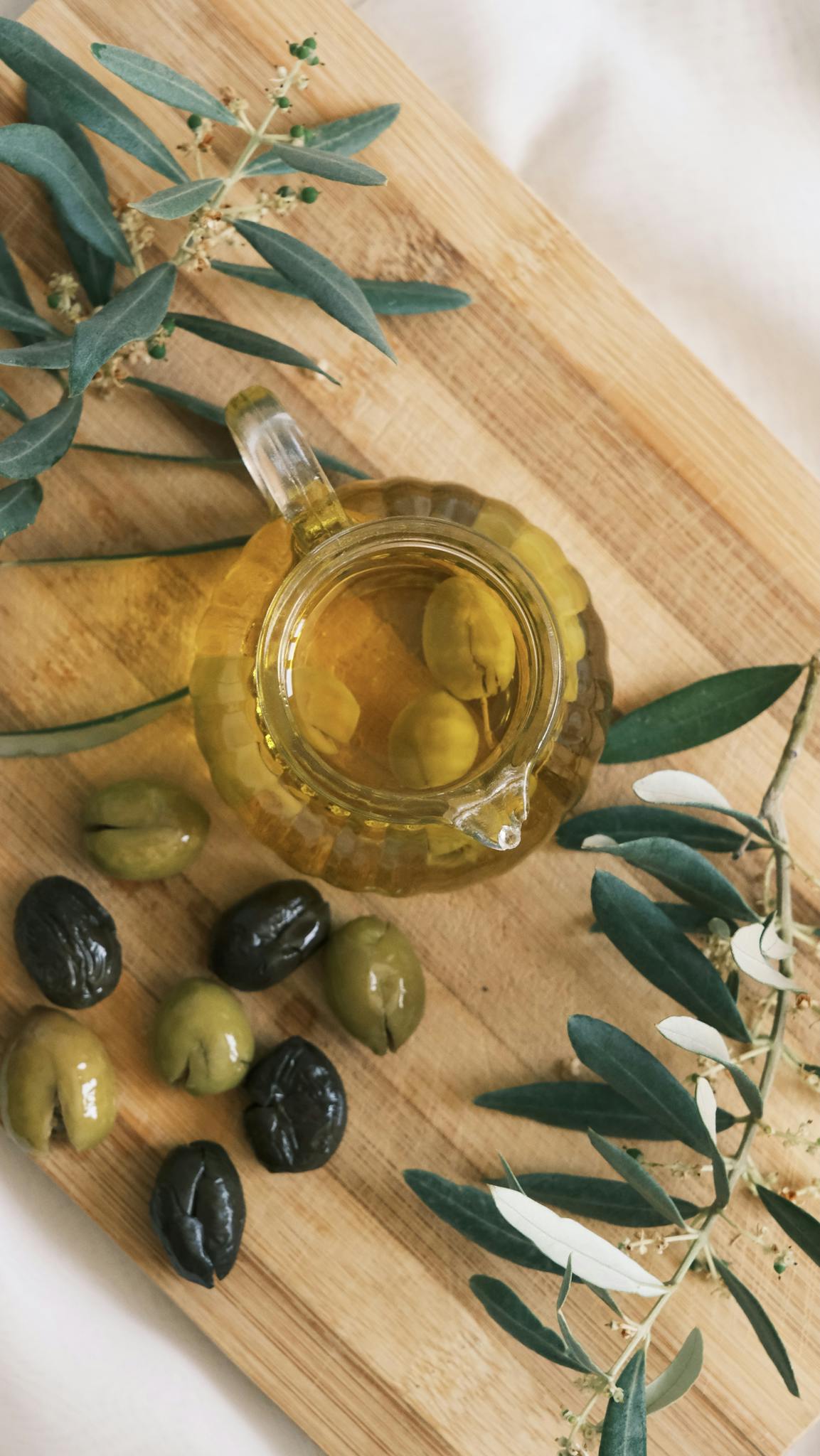 A top view of a cruet with olive oil and olives on a wooden cutting board.