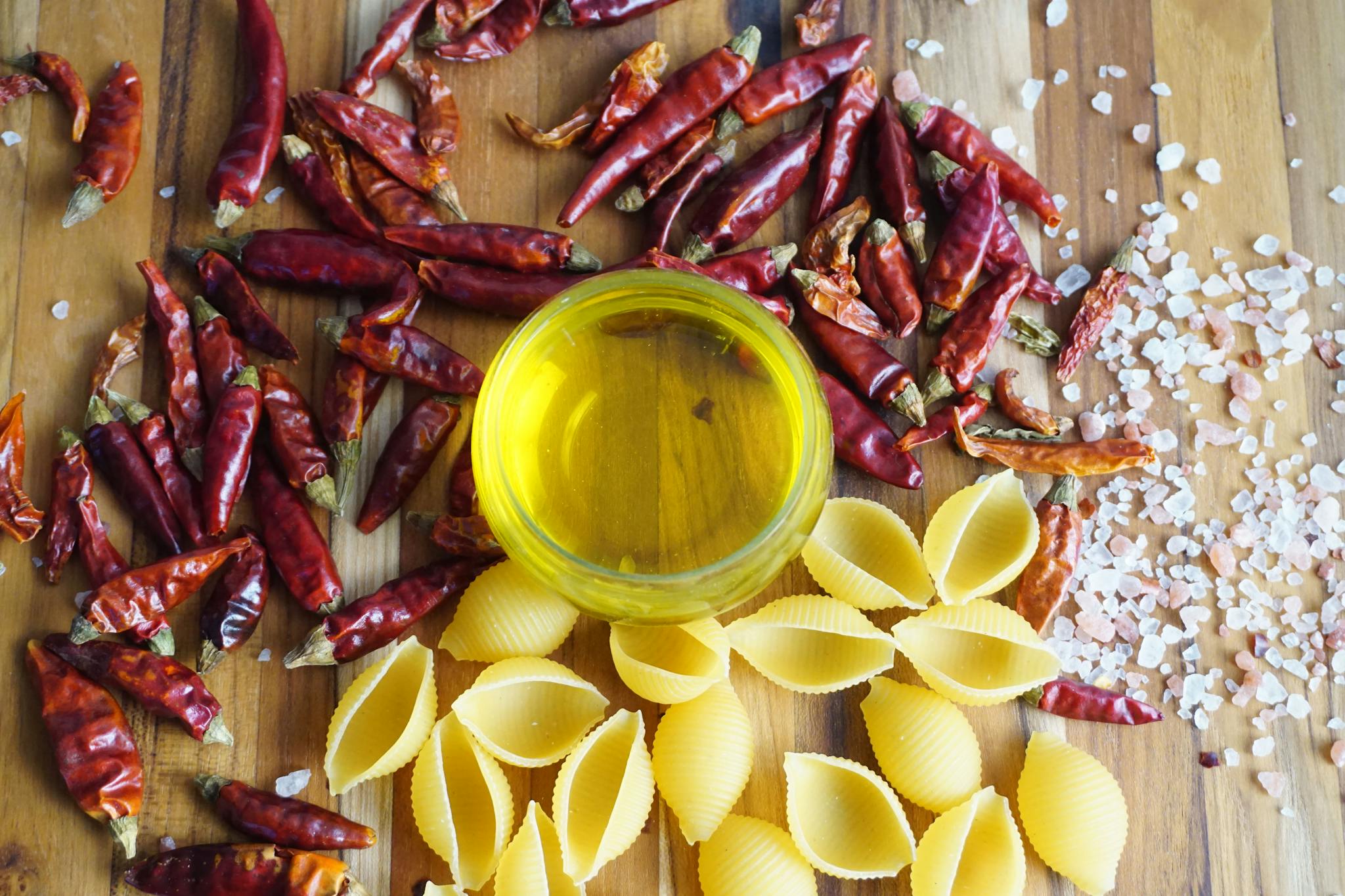 A vibrant display of chili peppers, pasta, and olive oil on a wooden board.