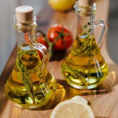 Close-up of herb-infused olive oil with fresh lemon and tomatoes on wooden surface.