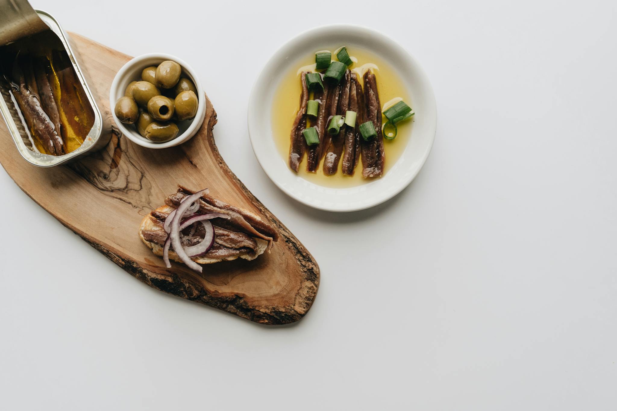 Delicious arrangement of anchovies and olives on a wooden board. Perfect food photography for culinary topics.