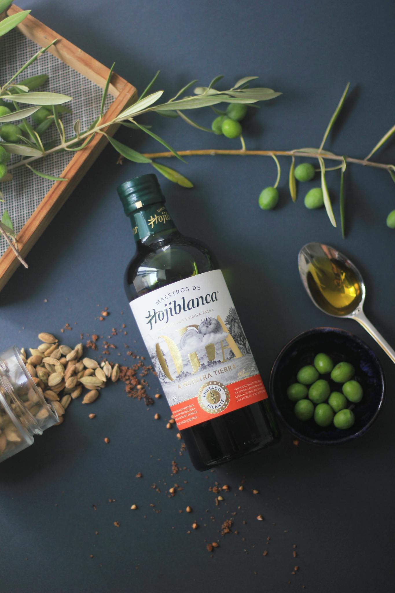 Top view of Hojiblanca olive oil bottle with fresh olives and spices for culinary use.